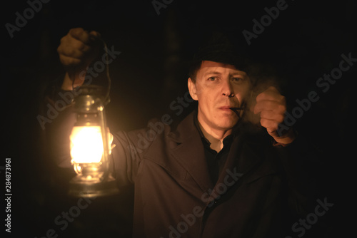 Detective agent with a kerosene lamp in hand is smoking his smoking pipe.
