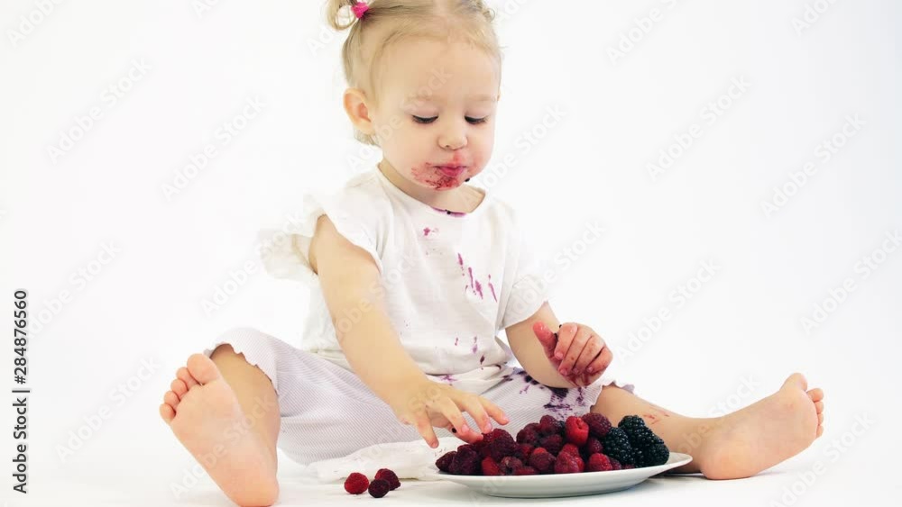 Smudged baby girl eats berries against white background Smudged baby girl eats berries against white background