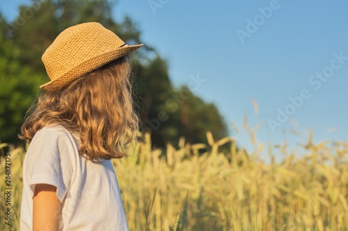 Girl child blonde in hat in wheat field, summer sunset