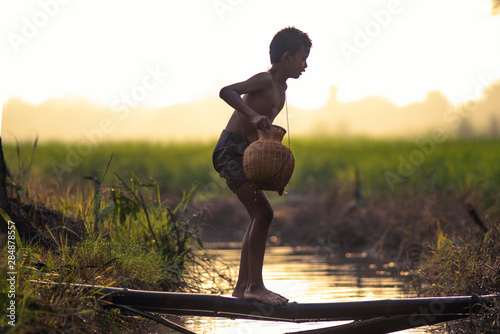 Asian little child fisherman holding fish trap walking along the river in the morning.