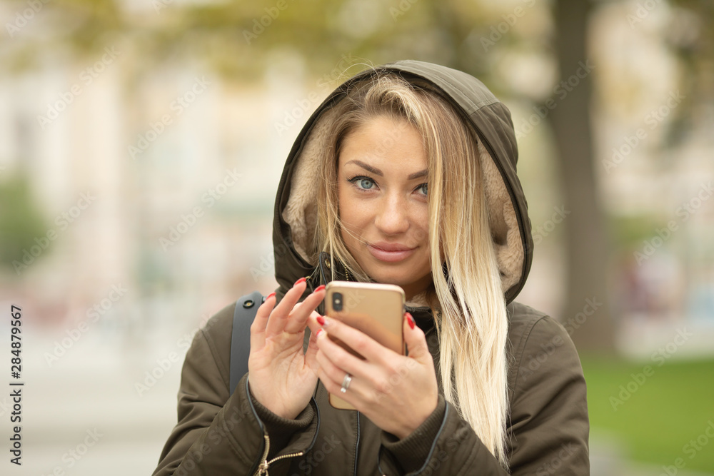 Young beautiful woman using her mobile phone at dusk in the city. Smiling girl sending message from cellphone in urban environment. Woman surfing the net with smartphone on autumn day in the street. Young beautiful woman using her mobile phone at dusk in the city. Smiling girl sending message from cellphone in urban environment. Woman surfing the net with smartphone on autumn day in the street.