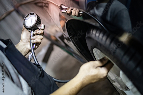 Male auto mechanic hand checking tire pressure in car repair garage. Automobile service and maintenance. Motor vehicle industry