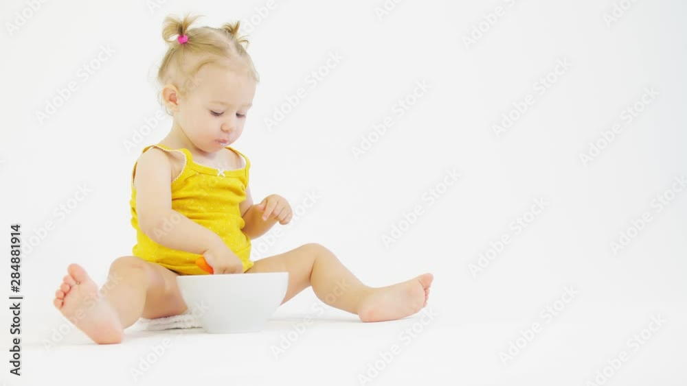 Blonde baby girl eats her breakfast on white background Blonde baby girl eats her breakfast on white background