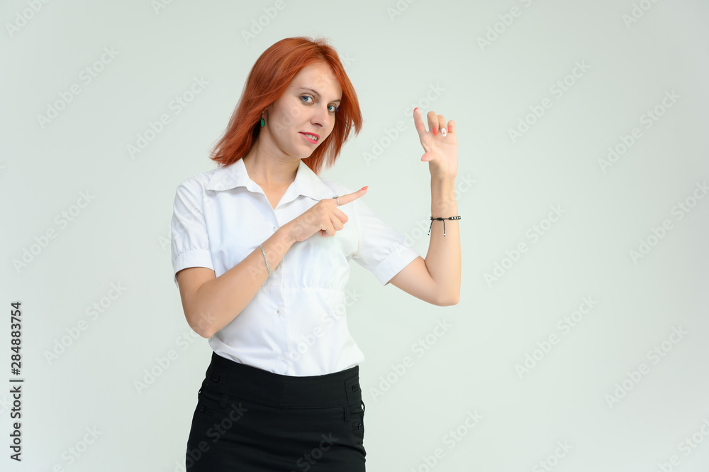 Fototapeta premium Photo Portrait of a cute girl woman with bright red hair manager in a white shirt on a white background in studio. He talks, shows his hands in front of the camera with emotions.