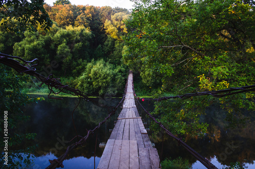 Suspension bridge over the river. Wooden suspension bridge in the summer in the village of Khotylevo, Bryansk