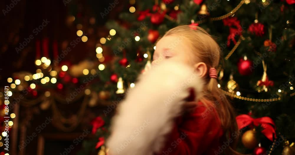 A pretty little girl takes off the Christmas cap in apartment with christmas lights and decorations. Merry Christmas, happy New Year. Miracle time. A pretty little girl takes off the Christmas cap in apartment with christmas lights and decorations. Merry Christmas, happy New Year. Miracle time.