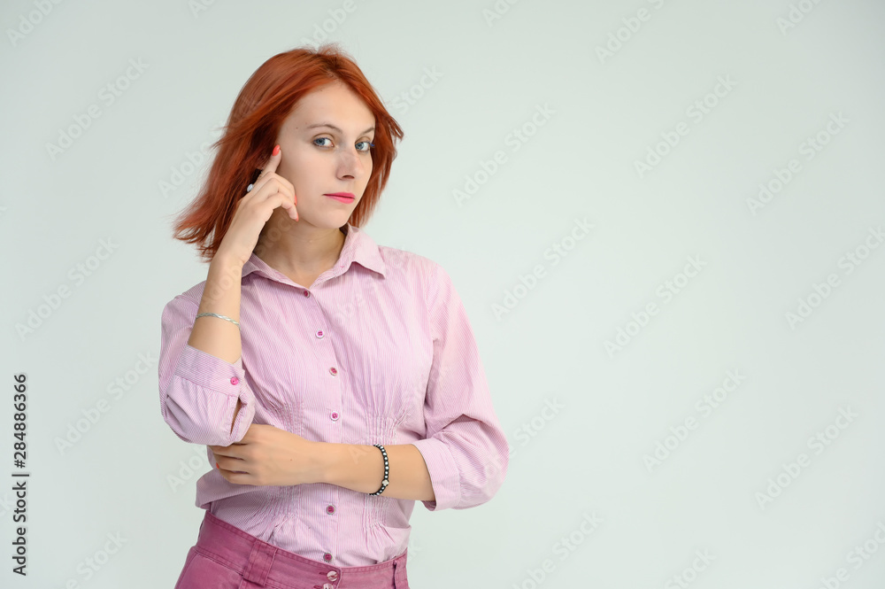 Photo Portrait of a cute girl woman with bright red hair manager in a pink shirt on a white background in studio. He talks, shows his hands in front of the camera with emotions. Photo Portrait of a cute girl woman with bright red hair manager in a pink shirt on a white background in studio. He talks, shows his hands in front of the camera with emotions.