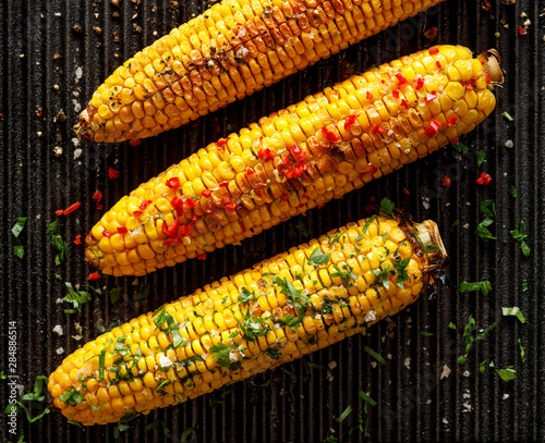 Grilled corn on the cob with butter, herbs, salt and aromatic spices on the grill plate, top view photo