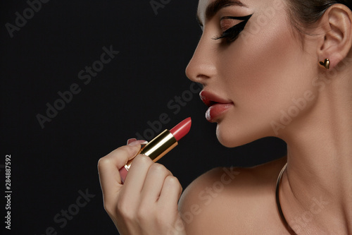 profile of brunette with sexy make-up holding a red lipstick in her hand