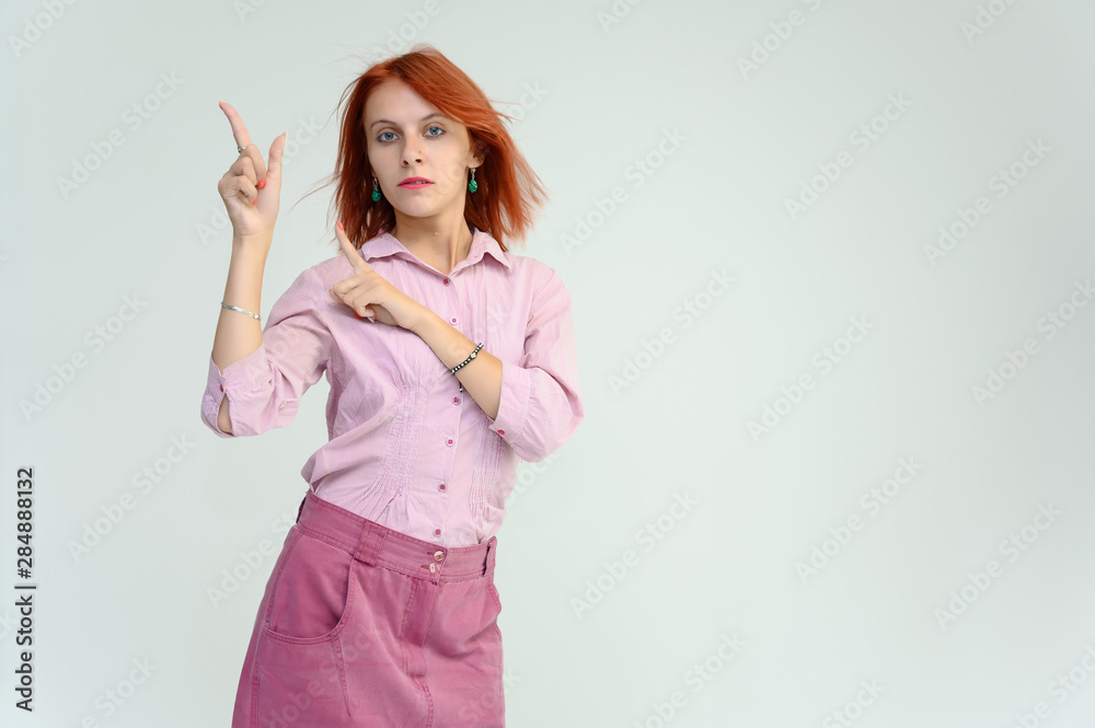 Photo Portrait of a cute girl woman with bright red hair manager in a pink shirt on a white background in studio. He talks, shows his hands in front of the camera with emotions. Photo Portrait of a cute girl woman with bright red hair manager in a pink shirt on a white background in studio. He talks, shows his hands in front of the camera with emotions.