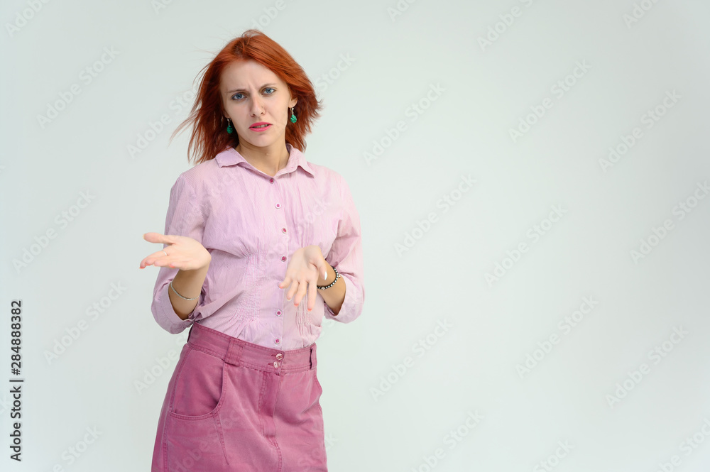 Photo Portrait of a cute girl woman with bright red hair manager in a pink shirt on a white background in studio. He talks, shows his hands in front of the camera with emotions. Photo Portrait of a cute girl woman with bright red hair manager in a pink shirt on a white background in studio. He talks, shows his hands in front of the camera with emotions.