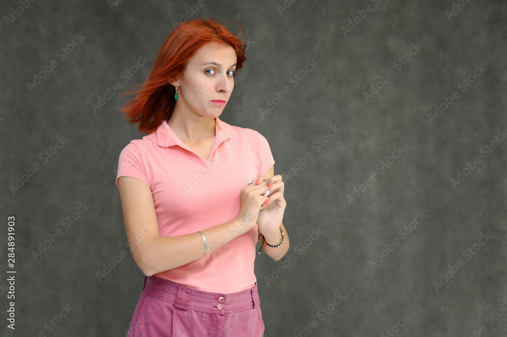 Photo Portrait of a cute woman girl with bright red hair in a peach t-shirt and pink skirt on a gray background in the studio. He talks, shows his hands in front of the camera with emotions. Photo Portrait of a cute woman girl with bright red hair in a peach t-shirt and pink skirt on a gray background in the studio. He talks, shows his hands in front of the camera with emotions.