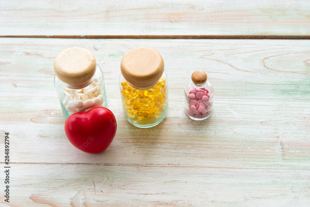 Colorful medicines in the glass bottles with red heart on the wooden table. Assorted pharmaceutical medicine or vitamine pills, tablets and capsules Colorful medicines in the glass bottles with red heart on the wooden table. Assorted pharmaceutical medicine or vitamine pills, tablets and capsules