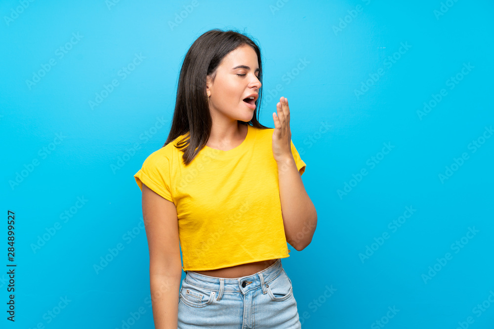 Young girl over isolated blue background yawning and covering wide open mouth with hand Young girl over isolated blue background yawning and covering wide open mouth with hand