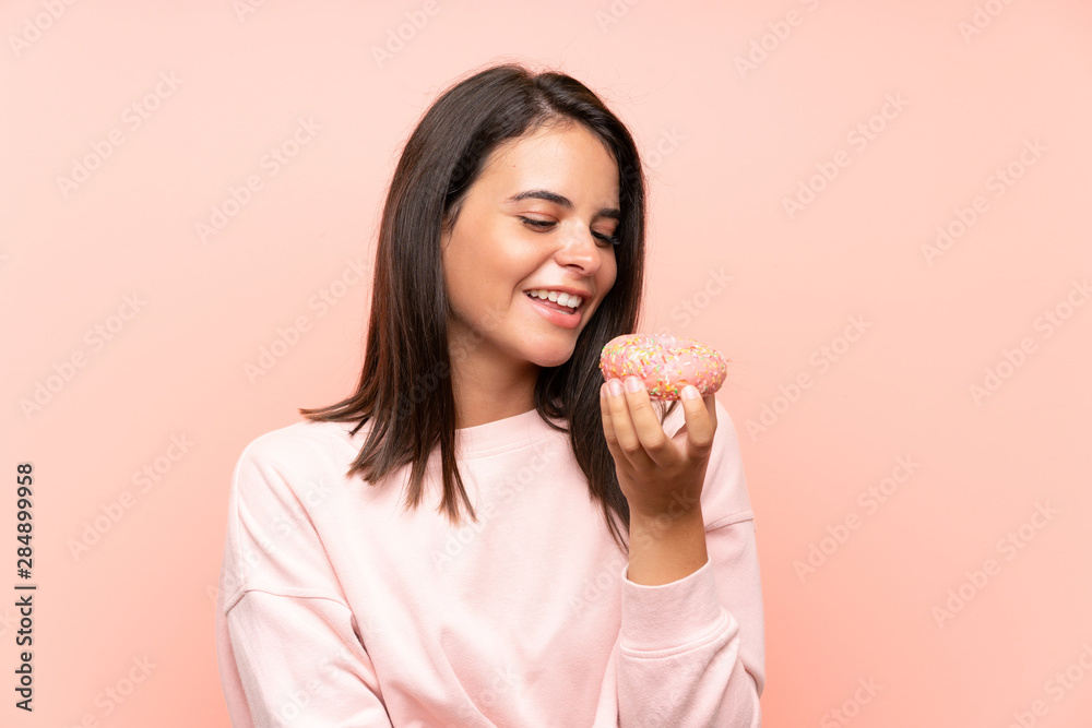 Young girl holding a donut over isolated pink background Young girl holding a donut over isolated pink background