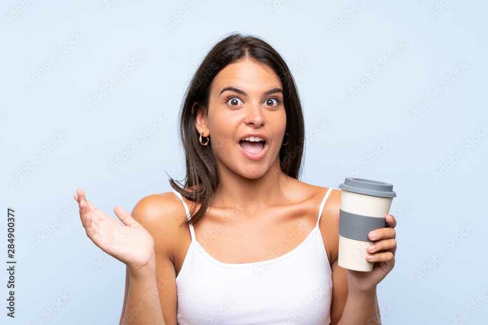 Young woman holding a take away coffee over isolated blue background with shocked facial expression Young woman holding a take away coffee over isolated blue background with shocked facial expression