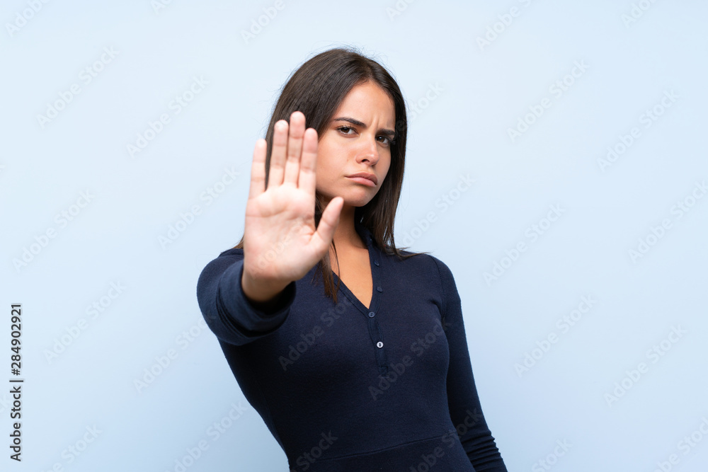 Young girl over isolated blue background making stop gesture with her hand Young girl over isolated blue background making stop gesture with her hand