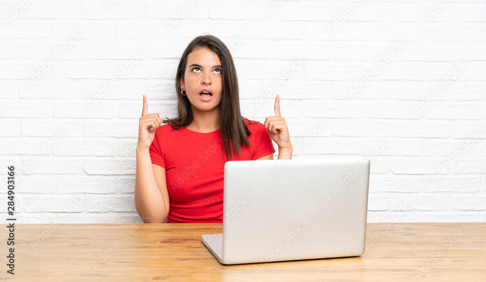 Young girl with pc in a table pointing with the index finger a great idea Young girl with pc in a table pointing with the index finger a great idea