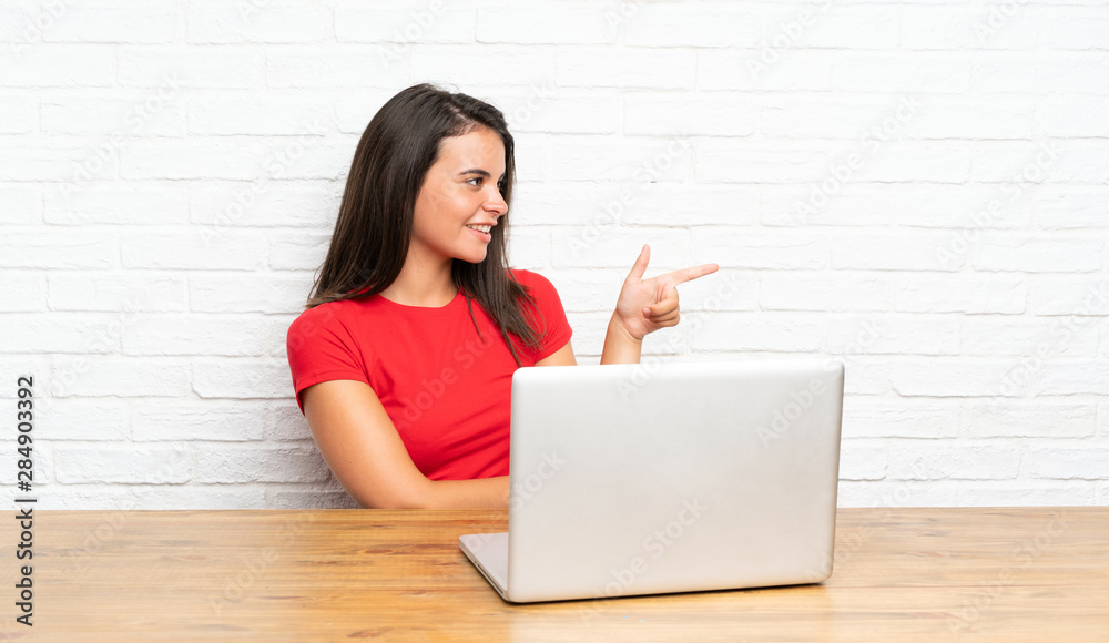 Young girl with pc in a table pointing finger to the side Young girl with pc in a table pointing finger to the side