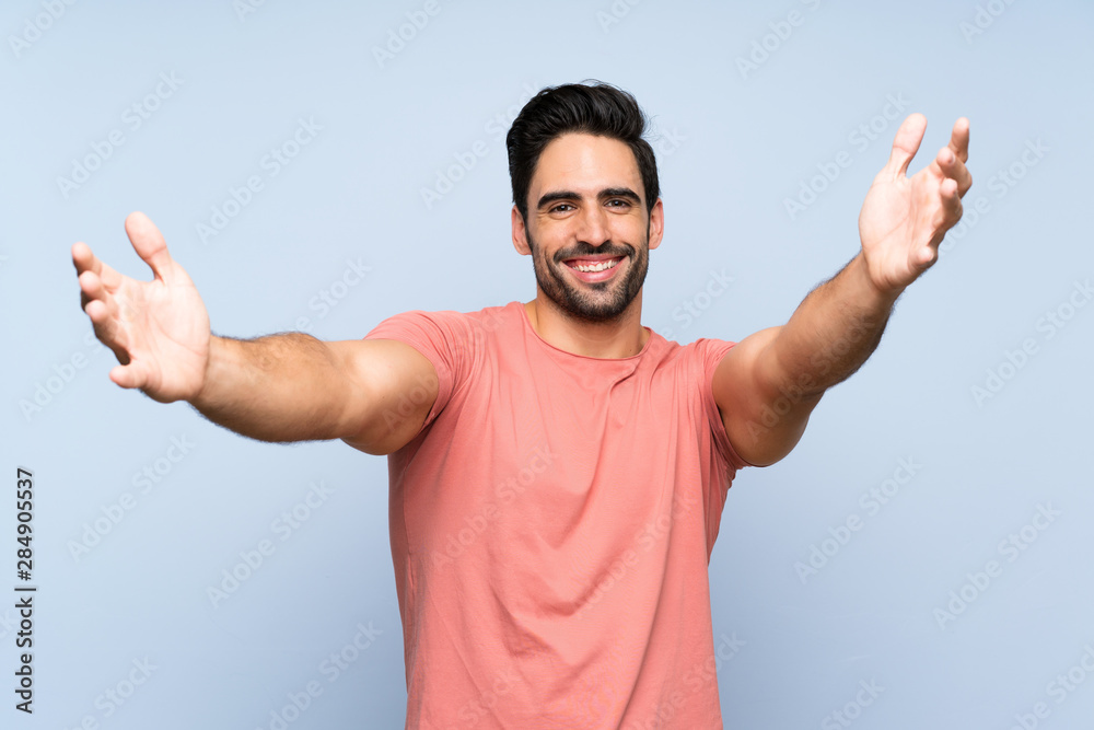 Handsome young man in pink shirt over isolated blue background presenting and inviting to come with hand Handsome young man in pink shirt over isolated blue background presenting and inviting to come with hand