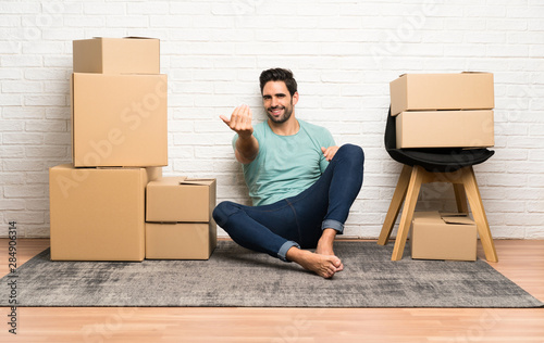 Handsome young man moving in new home among boxes inviting to come