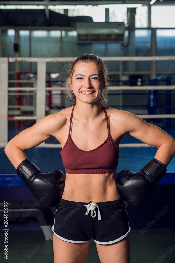 Strong woman in a black gloves standing in front of boxing ring