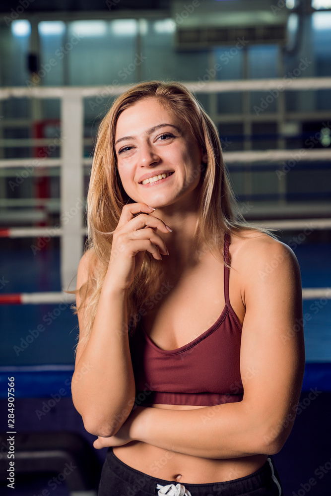 Young strong woman in red top standing in front of boxing ring and smiling Young strong woman in red top standing in front of boxing ring and smiling