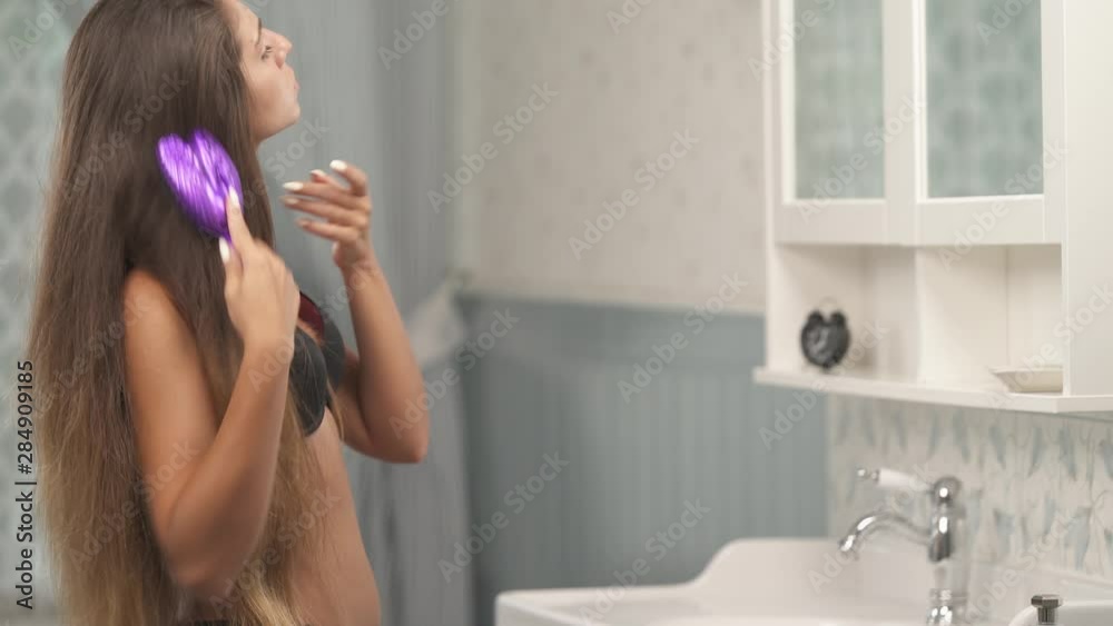 A side view of s beautiful slim woman in black bra combing her long hair in bathroom at home. Everyday care and beauty concept A side view of s beautiful slim woman in black bra combing her long hair in bathroom at home. Everyday care and beauty concept