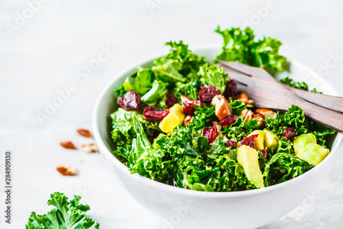 Green kale salad with cranberries and avocado in white bowl. Healthy vegan food concept.