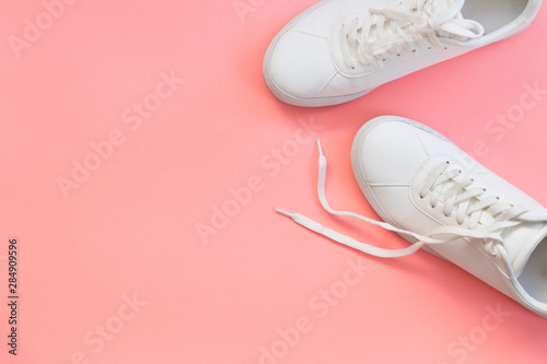 Fashion blog or magazine concept. White female sneakers on pink background. Flat lay, top view minimal background.