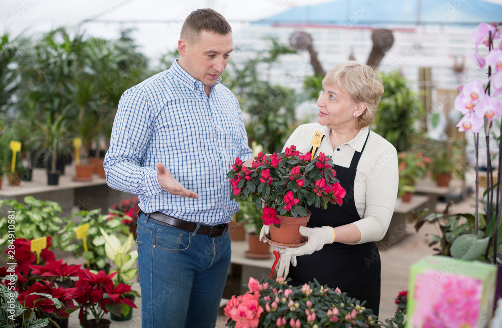 Adult woman is helping to man with choice of blooming flower