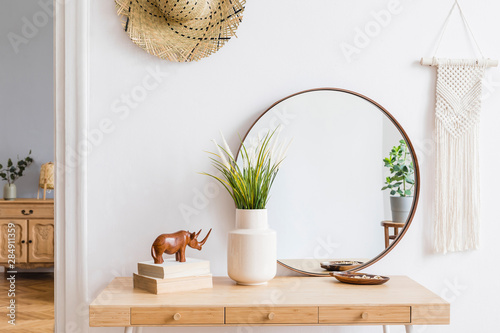 Foto Sunny boho interiors of apartment with mirror, dressing table, furnitures, flowers, plants, rattan hat, sculpture, macrame and design accessories