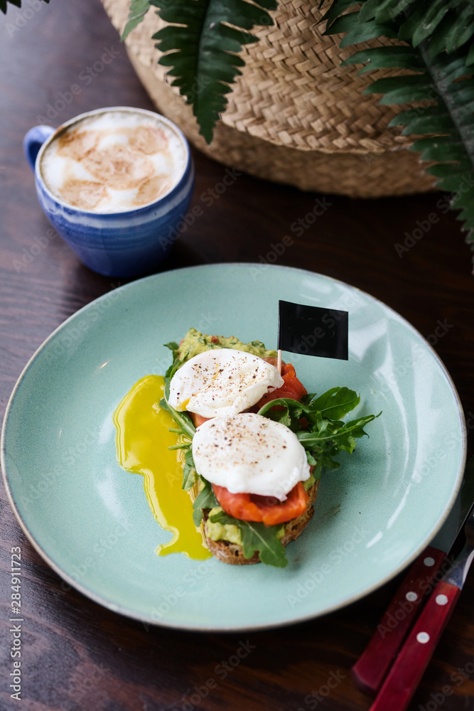 Hot toast with salmon, poached egg, herbs and avocado on a plate with a black copy space flag on a skewer Hot toast with salmon, poached egg, herbs and avocado on a plate with a black copy space flag on a skewer