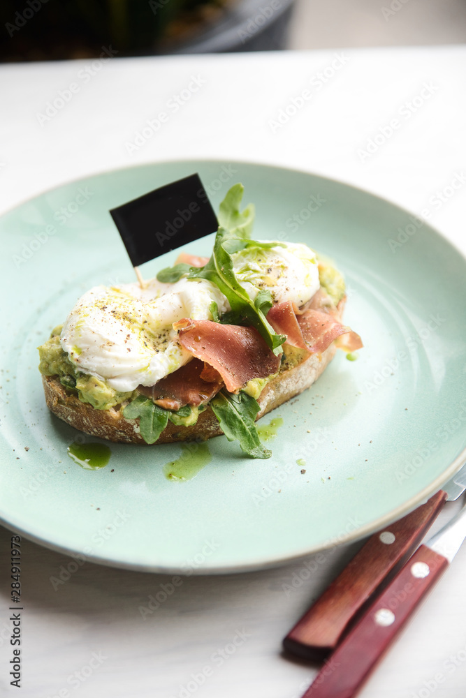 Hot toast with jamon, poached egg, herbs and avocado on a plate with a black copy space flag on a skewer