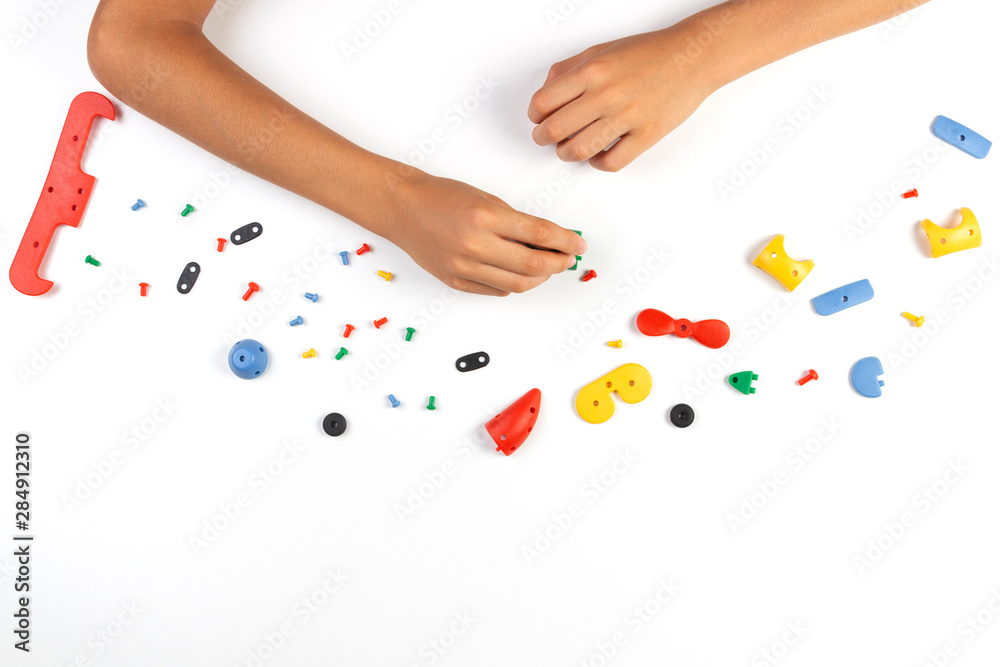 Kid hands playing with colorful plastic parts of constructor on white table. Top view Kid hands playing with colorful plastic parts of constructor on white table. Top view
