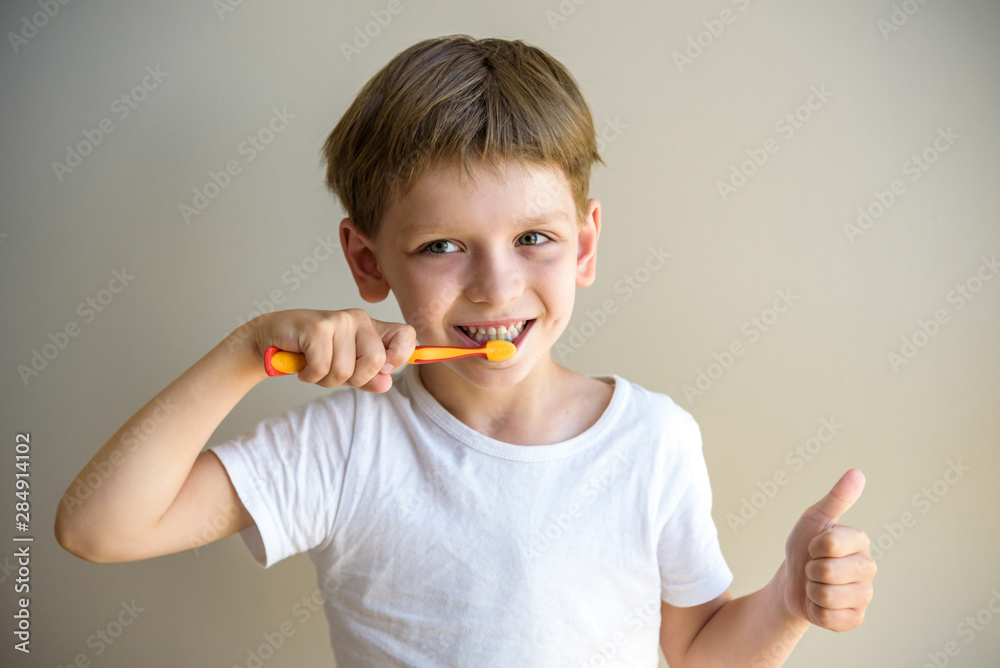 A cute little boy is brushing his teeth with a toothbrush. On a pure white T-shirt in which he is dressed you can make an advertising inscription. The concept of children's health, medicine A cute little boy is brushing his teeth with a toothbrush. On a pure white T-shirt in which he is dressed you can make an advertising inscription. The concept of children's health, medicine
