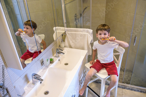 A cute little boy is brushing his teeth with a toothbrush. On a pure white T-shirt in which he is dressed you can make an advertising inscription. The concept of children's health, medicine