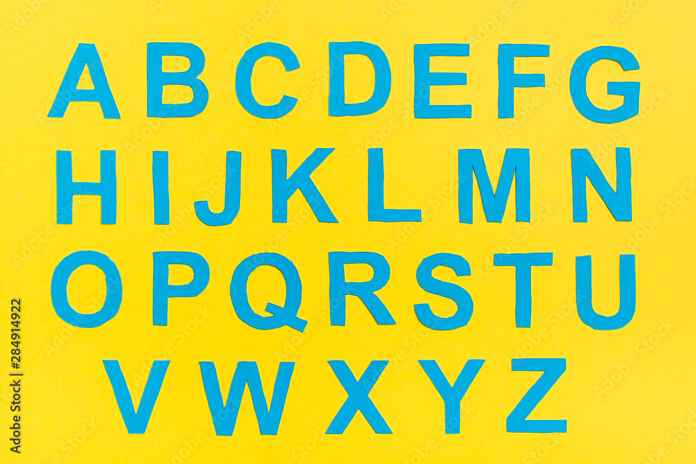 The letters of the English alphabet are cut from blue cardboard on a yellow background