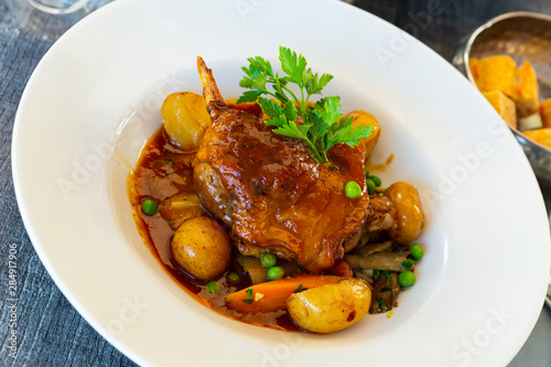 Roasted duck leg with baked potatoes, green peas, parsley and tomatoes. French cuisine
