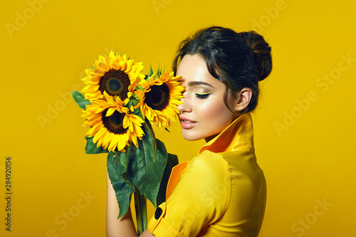 A girl in a yellow dress holds in her hands a bouquet of yellow sunflowers. photo