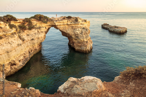 Albandeira Arch. Natural arch over the sea near Albandeira beach in the Algarve, Portugal in the late afternoon with a woman over the arch.