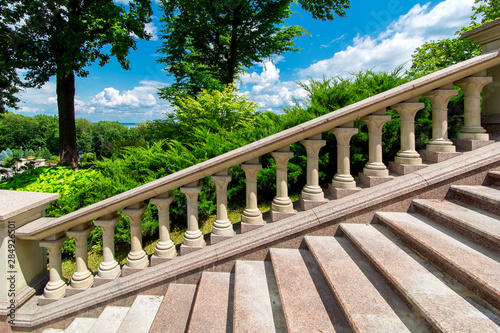 Fototapeta stone railing with balustrades at the granite staircase in the backyard with green plants on a sunny day with a blue sky, nobody