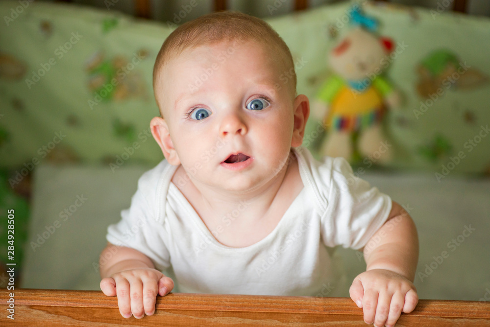 Cute little baby standing in a bed. Smiling child playing in bed. Kid portrait at nursery. Happy childhood concept Cute little baby standing in a bed. Smiling child playing in bed. Kid portrait at nursery. Happy childhood concept