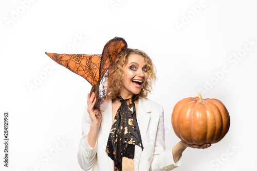 Witch. Hag. Trick or treat. Woman posing with Pumpkin. Beautiful smiling woman in witches hat and costume holding pumpkin. Blonde girl with Pumpkin. Jack-o-lanterns. Happy Halloween.