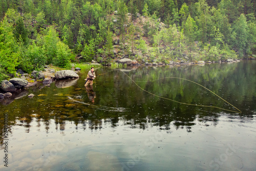 Fisherman man in mountain river in boots fly fishing salmon, morning. Aerial top view