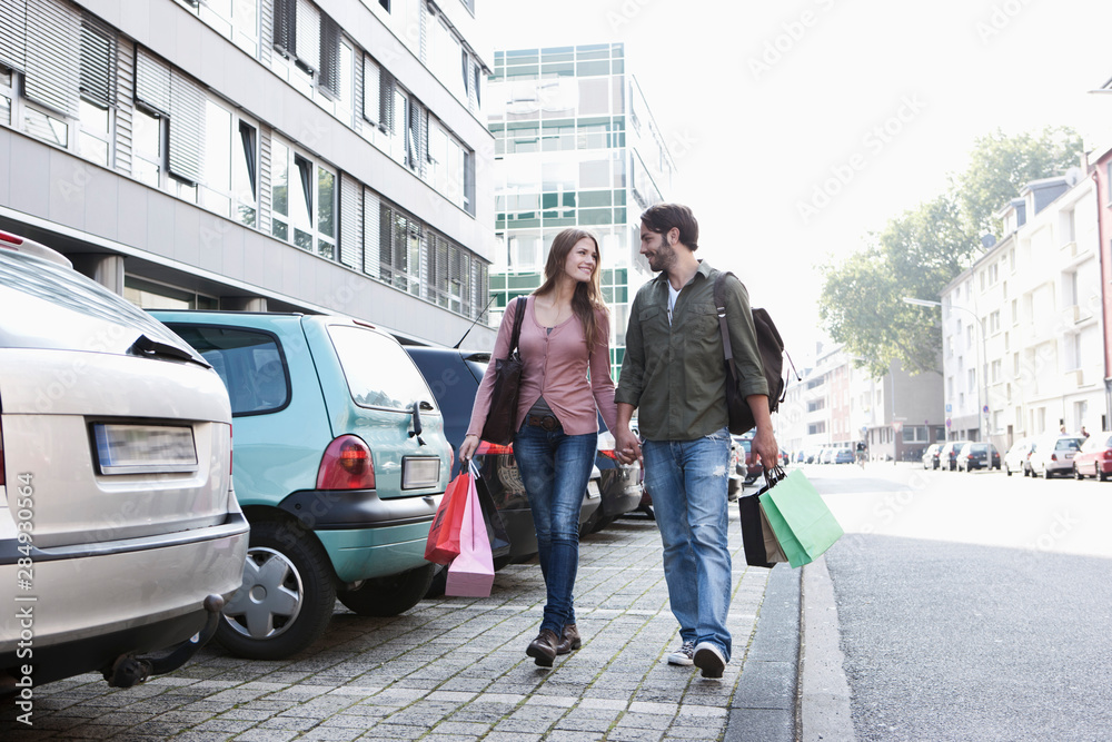 Germany, Cologne, Young couple with shopping bags near parking lot, smiling