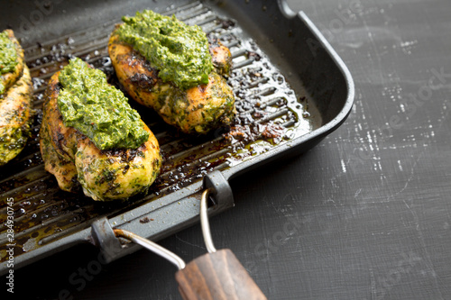 Ready-to-eat chimichurri chicken breast in a grilling pan on a black background, side view. Close-up. Copy space.