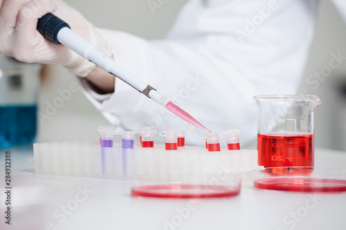 Germany, Bavaria, Munich, Scientist pouring red liquid in test tube for medical research in laboratory photo