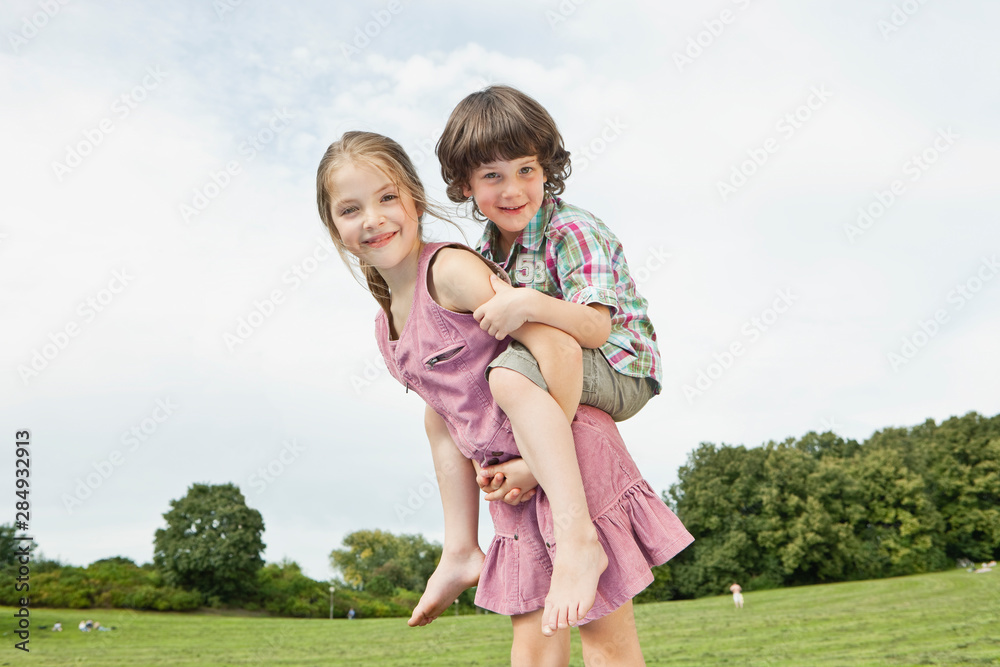 Germany, Bavaria, Girl giving piggy back ride to boy in park, smiling, portrait Germany, Bavaria, Girl giving piggy back ride to boy in park, smiling, portrait