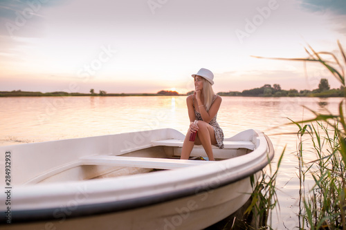 Young woman in a dress sitting on the boat and enjoying in a beautiful sunset while drinking beer © Jovica Varga